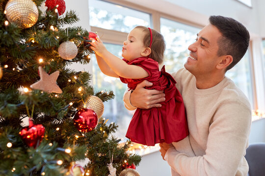 winter holidays and family concept - happy middle-aged father and baby daughter decorating christmas tree with ball at home