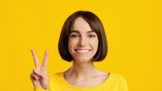 Happy Woman Gesturing V-Sign Posing On Yellow Studio Background