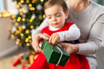 christmas, winter holidays and family concept - close up of grandmother and baby granddaughter opening gift box at home