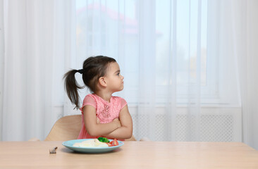 Cute little girl refusing to eat her breakfast at home, space for text