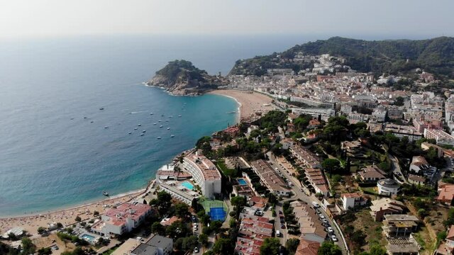Drone view of the fortress with scenic sea views in Tossa de Mar. Drone shot of a municipality in Spain. People are relaxing on a sandy beach in Spain. Spa town near the Mediterranean Sea