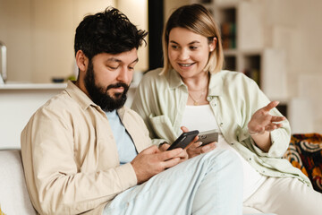 White couple using cellphones while sitting on couch at home