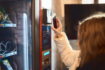 Woman paying for product at vending machine using smartphone