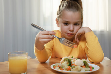 Cute little girl refusing to eat vegetable salad at home