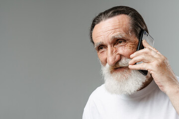Obraz premium European senior man with beard smiling while talking on mobile phone