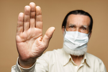 European senior man in face mask showing stop gesture at camera