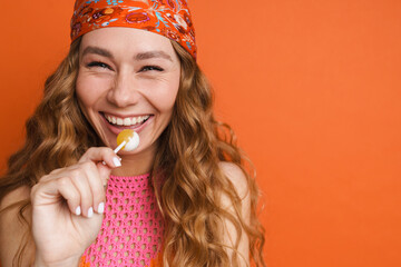 Young ginger woman in bandana laughing while posing with lollipop