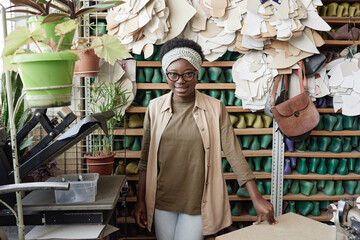 Portrait of African young shoemaker smiling at camera while standing in the workshop with shoelast on the shelves in the background