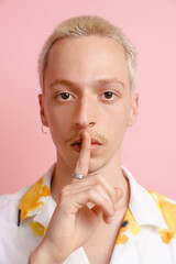 Young blonde man looking at camera and showing silence gesture