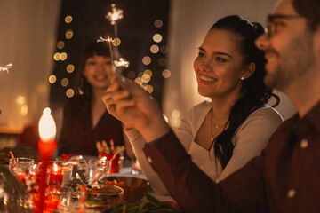 holidays and celebration concept - multiethnic group of happy friends with sparklers having christmas dinner at home