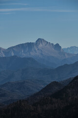 Beautiful panoramic landscape view of mountains on warm sunny autumn day. Blue sky and white clouds. In distance, steep cliffs and silhouettes of large snow capped mountain peaks.