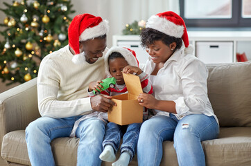 family, winter holidays and people concept - happy african american mother, father and little son opening gift box with toy car at home on christmas