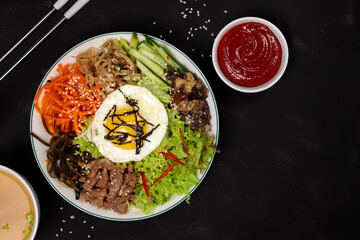 Pibimpap, a popular dish from Korean cuisine.Boiled rice with various toppings, served with broth and sauce. Top view on a black background
