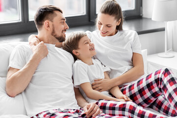 Obraz premium family, rest and people concept - happy mother, father and little son in matching pajamas sitting in bed in morning