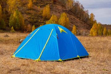 Blue tent near mountain river with colorful forest on background.