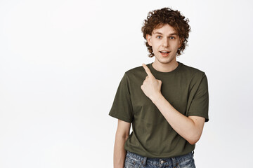 Image of young curly man pointing upper left corner, looking curious, asking question about sale...