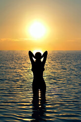girl stands in sea water in the rays of the setting sun