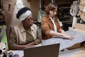 Two women sitting at the table and working in team, they packing boxes in the workshop