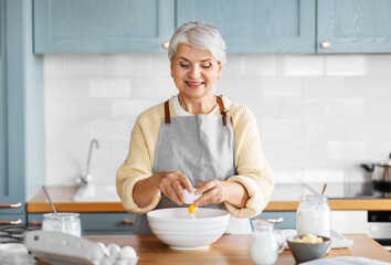 people and culinary concept - happy smiling woman cooking food on kitchen at home and breaking egg