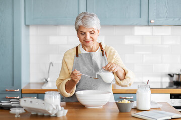 people and culinary concept - happy woman cooking food on kitchen at home and pouring milk or cream...