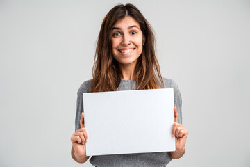 Naklejka premium Portrait of the caucasian overjoyed young woman holding blank paper or billboard while feeling happy isolated on white background