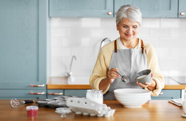 people and culinary concept - happy smiling woman cooking food on kitchen at home and adding sugar