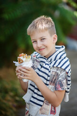 Cute blonde boy eating shrimp roll at fast food restaurant. Unhealthy meal for kids. Junk food. 