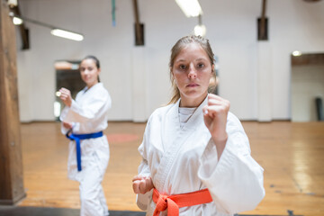 Obraz premium Motivated young women at karate training. Attractive women in white clothes with blue and red belts warming up before training. Sport, healthy lifestyle concept