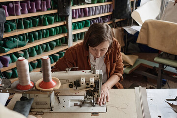 Shoemaker sitting at the table and using sewing machine in her work, she sewing new shoes