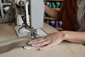 Close-up of seamstress sitting at the table and sewing clothes on sewing machine