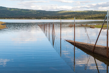A wire fence plunges into a lake