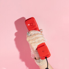 Creative layout with hand in white lace glove  holding red retro telepfone handset on pastel pink...