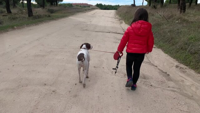 Unrecognizable little girl in a red coat walking with her dog along a path through a forest