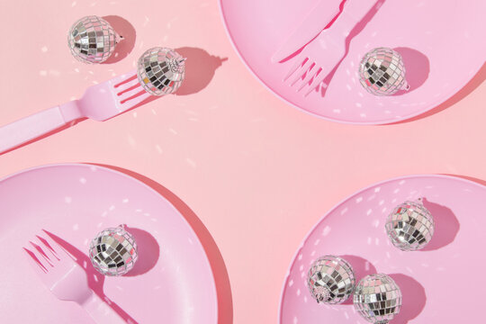 Christmas and New Year creative layout with plates, forks, knifes and disco ball decorations on pastel pink background. 80s or 90s aesthetic fashion restaurant concept. New Year dinner  idea.