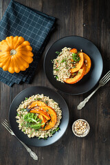 Roasted pumpkin salad with quinoa, kale, pine nuts in a black plate on wooden background, top view
