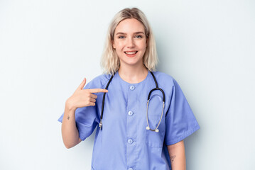 Young nurse woman isolated on blue background person pointing by hand to a shirt copy space, proud...