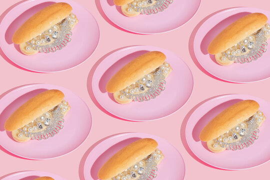 Creative pattern with luxury jewelry in hot dog buns on pink plates on pastel pink background.  80s or 90s retro aesthetic fashion food concept. Minimal surreal restaurant or fast food idea.
