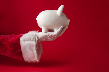 Santa Claus holding a Christmas piggy bank money box. Festive saving concept