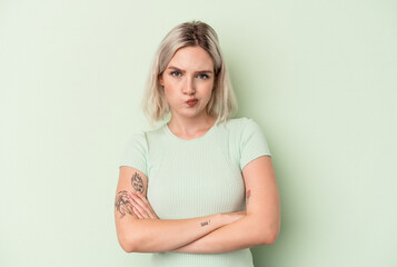 Young caucasian woman isolated on green background frowning face in displeasure, keeps arms folded.