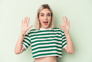 Young caucasian woman isolated on green background receiving a pleasant surprise, excited and raising hands.