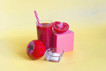 Natural tomato juice in a glass container with a decor of tomatoes, salt and a colored cube on a light background