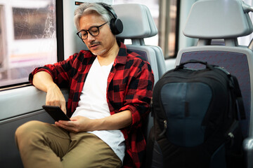 Senior man traveling by train. Man listening the music while enjoying in travel