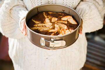 Woman's hands with a sweater holding a freshly baked cake in the pan.