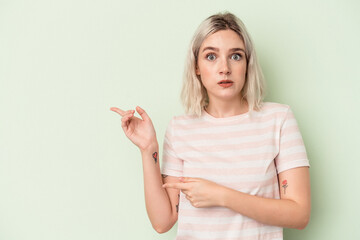 Young caucasian woman isolated on green background shocked pointing with index fingers to a copy space.