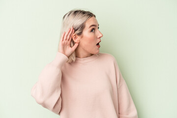 Young caucasian woman isolated on green background trying to listening a gossip.