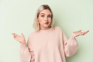 Young caucasian woman isolated on green background doubting and shrugging shoulders in questioning...