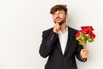Young mixed race man holding bouquet of roses isolated on white background looking sideways with...