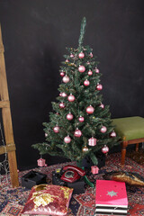 a green elegant Christmas tree with pink balls stands in a room on a red palace and on a dark background.