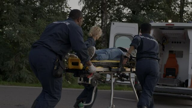 Paramedics running to ambulance car with man on stretcher