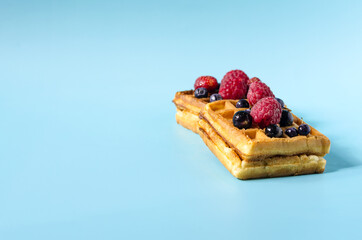 Baking soft waffles with black and red berries on a blue background of bright light. Homemade cakes waffles on a colored background copy space